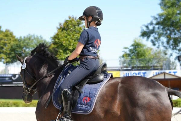 TOTAL EquiPro Sponsored Rider Kendra Victoria Li, Dressurreiterin des Hong Kong Jockey Clubs, von hinten gesehen. Ihr Pferd trägt unsere Schabracke, sie ein TOTAL EquiPro Polohemd.
