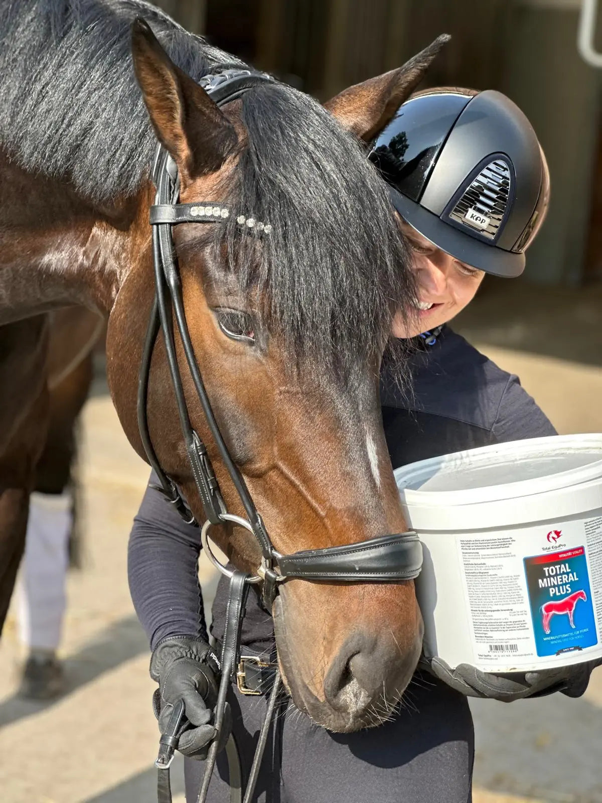 Sussi Steinberg mit Pferd und TOTAL Mineral Plus Eimer im Stall.